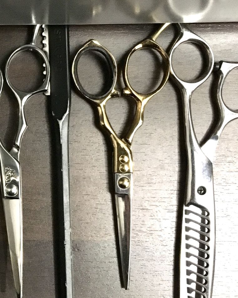 Several pairs of professional haircutting scissors and thinning shears hanging from a magnetic strip.
