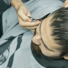 Close view of shears taking a line along a caped client's hairline.
