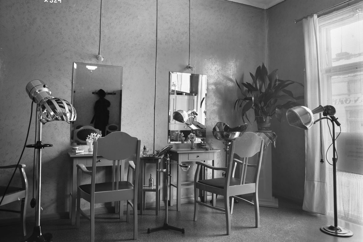 A 1934 hairdressing room with two hood dryers on stands, tall mirrors and a row of chairs.