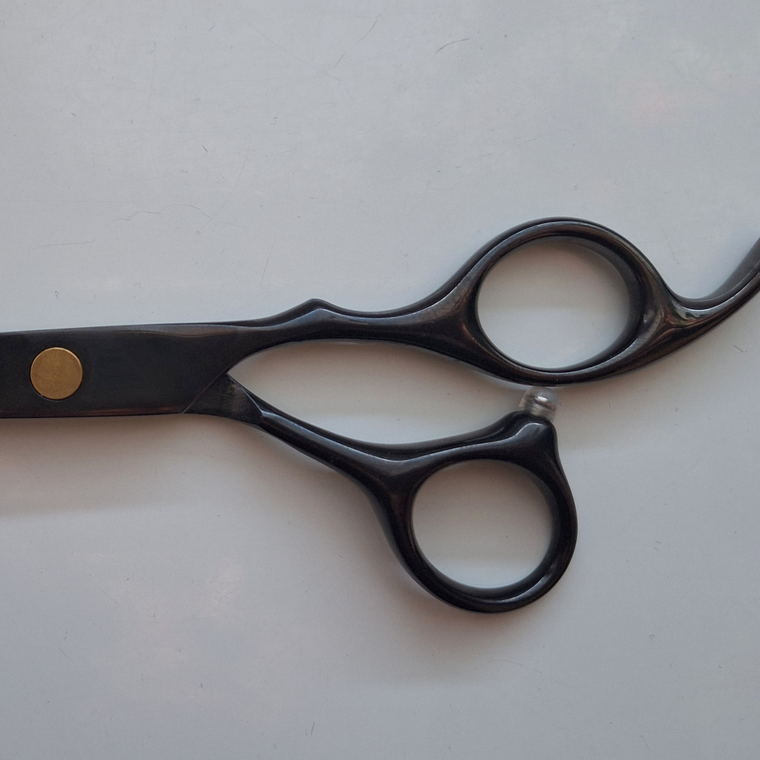 A pair of haircutting shears with black handles resting on a pale grey surface.