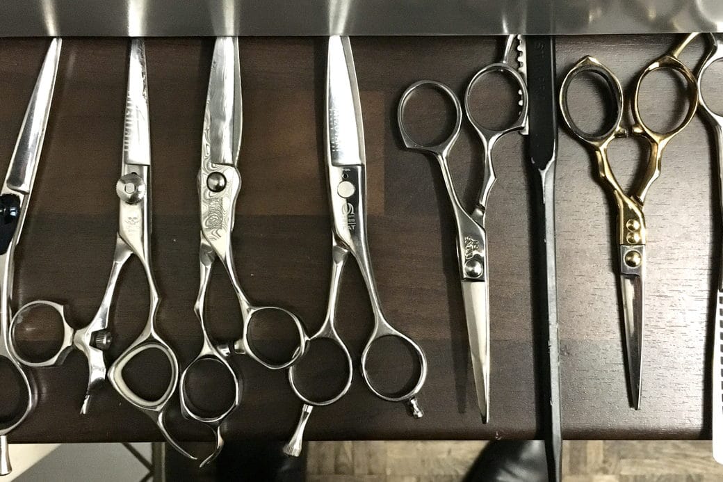 Professional haircutting shears arranged in a row against a dark work surface.