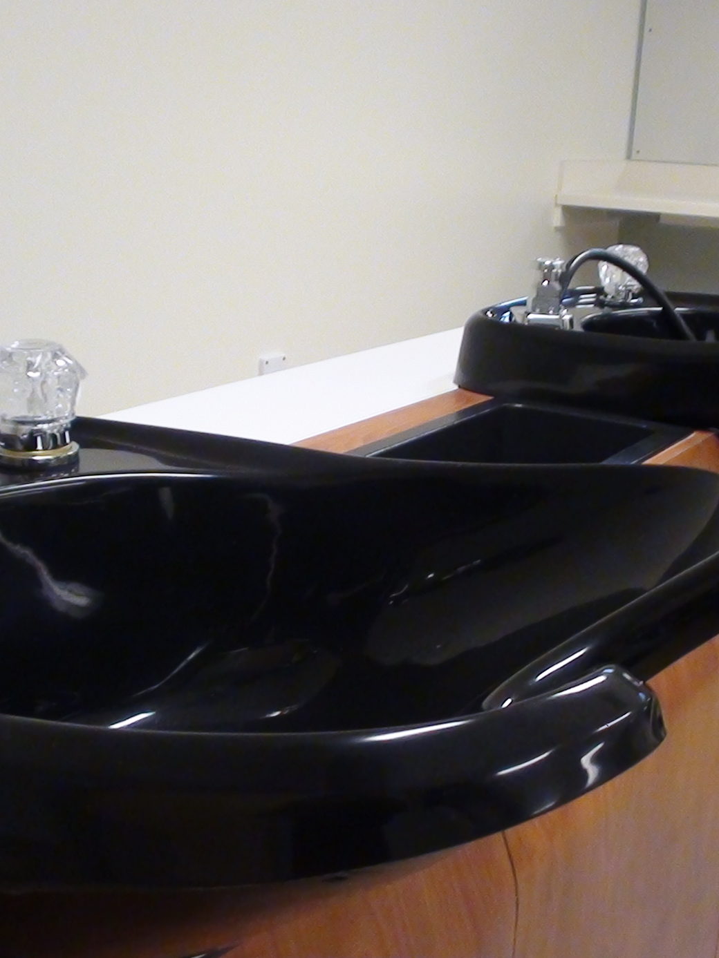 A black ceramic backwash basin set into a wooden unit, empty and ready at the wash station.