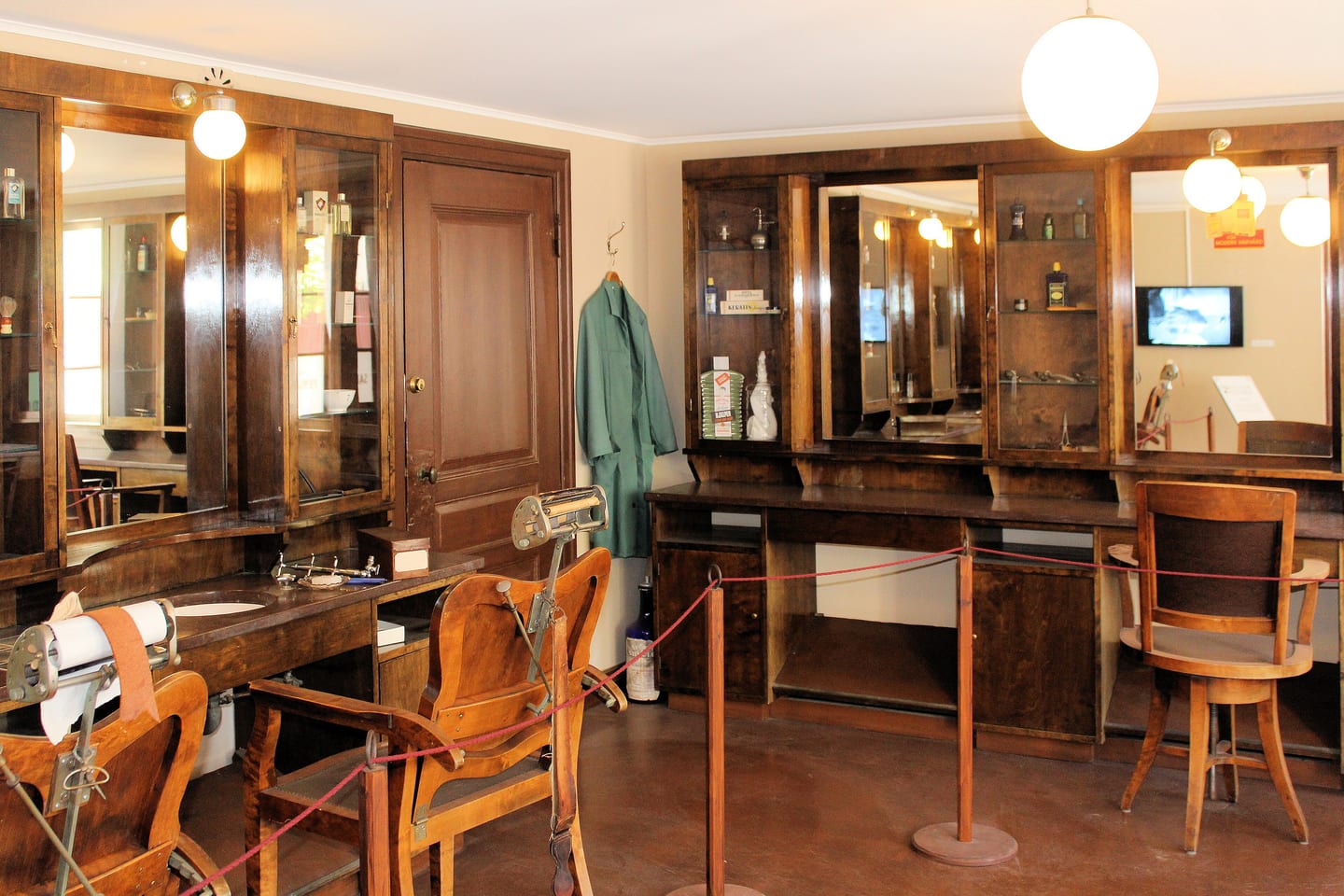 A salon interior with dark wood mirrored cabinets, chairs and a gown hanging by the wall.