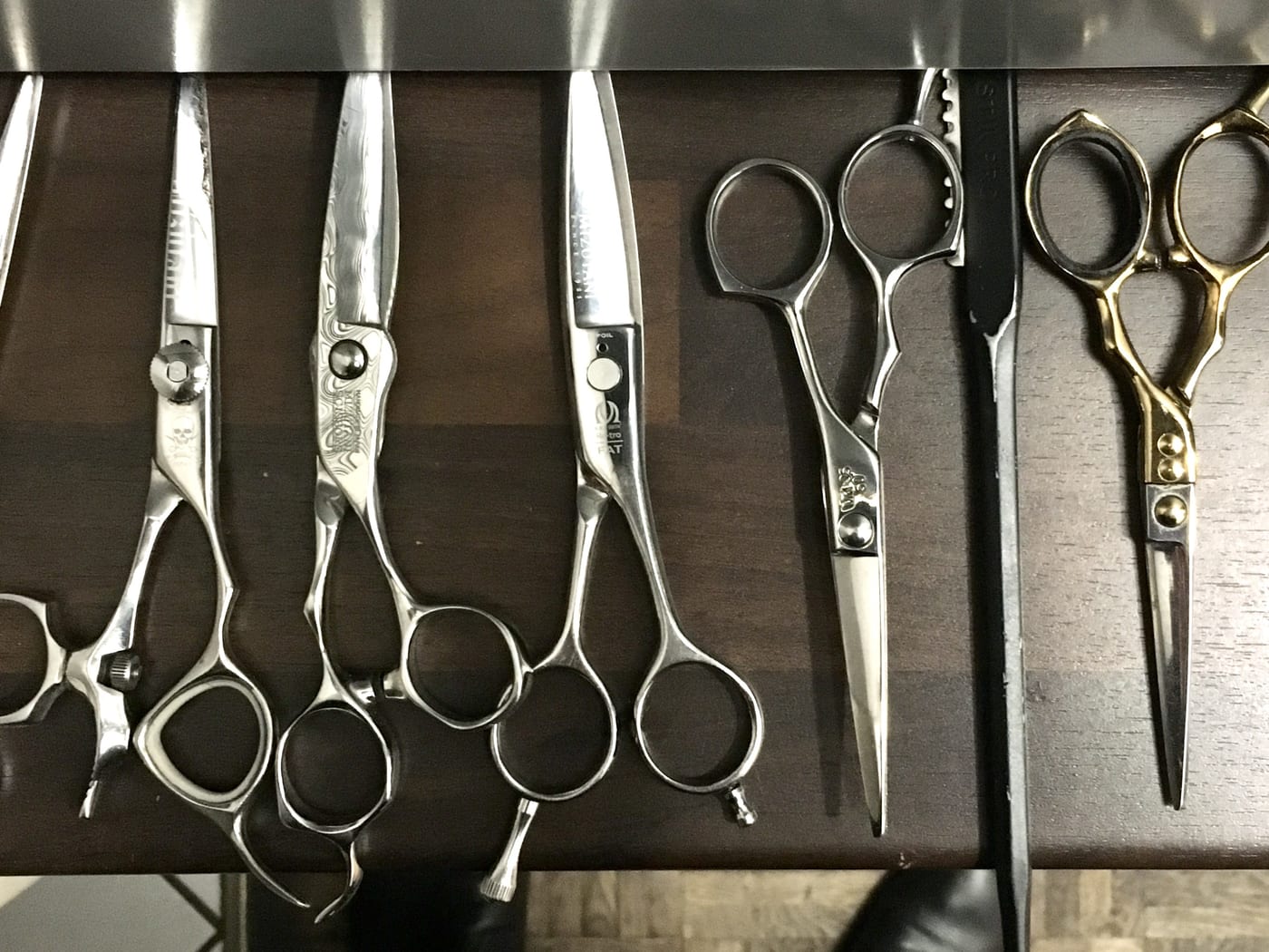 A row of professional haircutting scissors laid out on a dark counter.