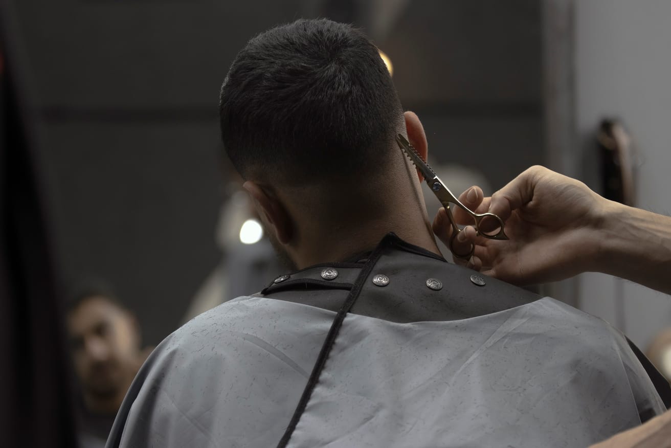 A stylist cutting hair at the back of a client's head, seen from behind.