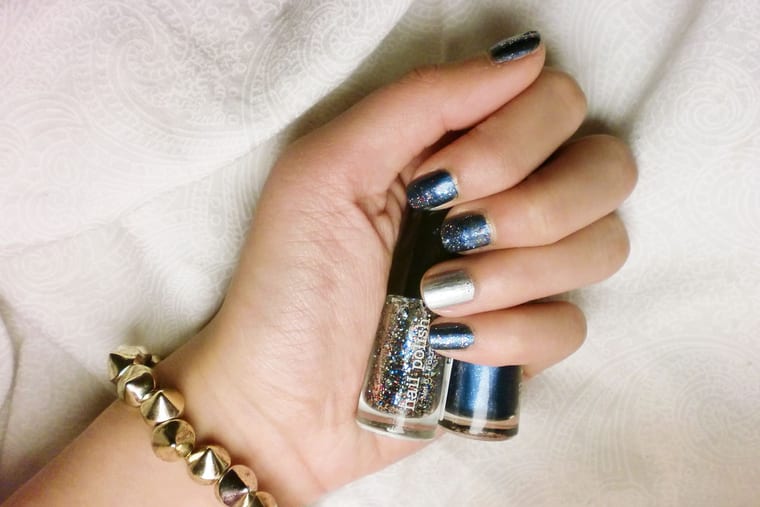 A hand with nails painted in silver and dark glitter, held against a dark background.