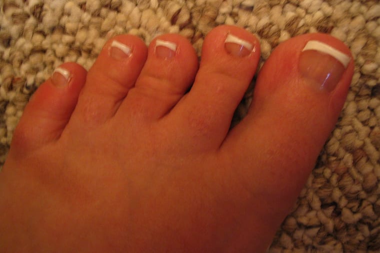 Two feet with toenails finished in a pale french style, photographed against a light floor.