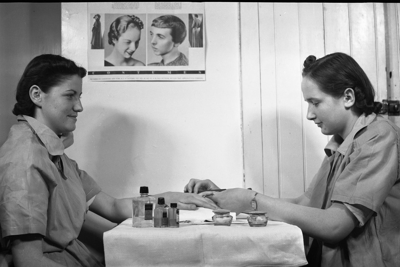 An archive photograph from 1938 of a manicure being given at a small cloth-covered table.