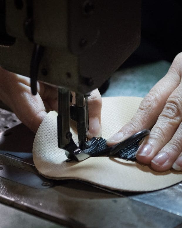A person's hands guiding cloth beneath a sewing machine needle, photographed from the side. No face is visible.