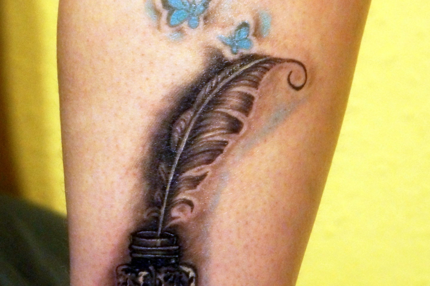 A finished feather-and-inkwell tattoo photographed close on the calf.