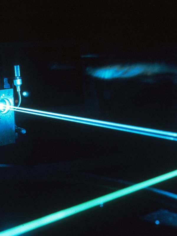 Teal laser beams crossing an optical bench in a darkened room
