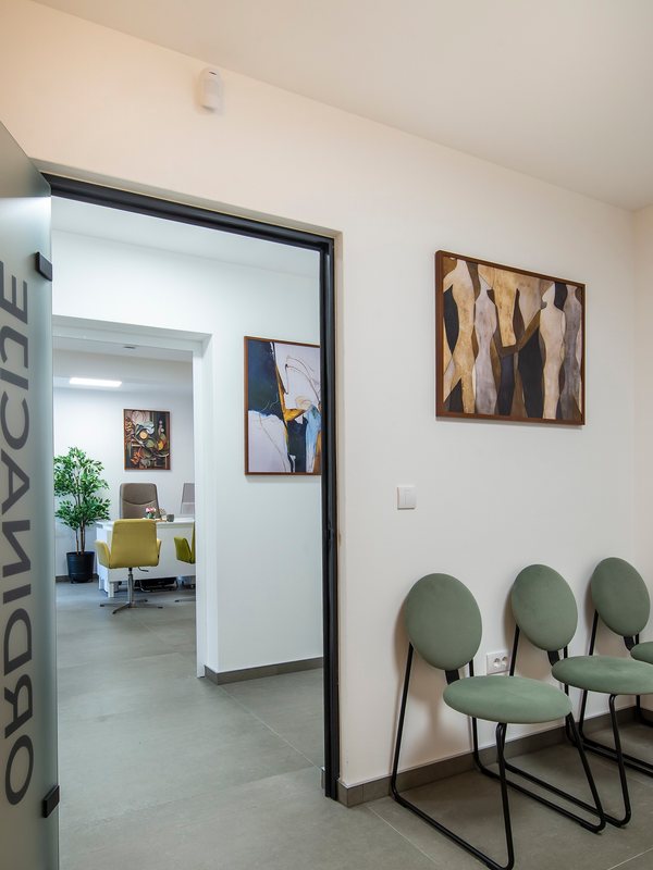 Waiting area with upholstered chairs beside an open consulting-room door
