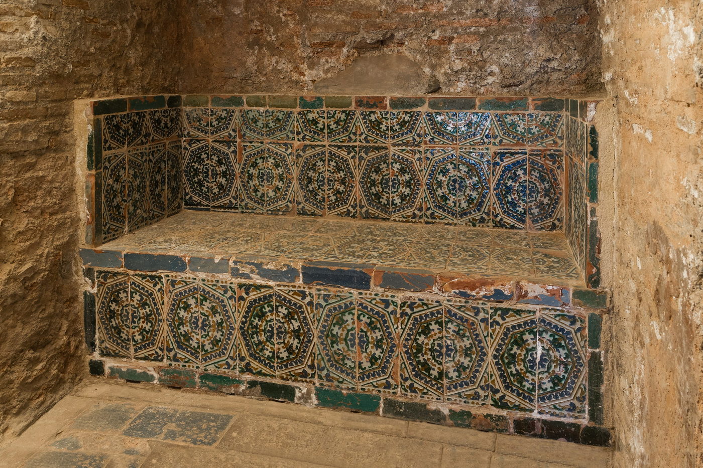 A long tiled bench set into a stone alcove in the steam room, the tilework patterned in green and blue.