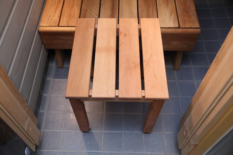 A plain wooden stool standing on a tiled sauna floor.
