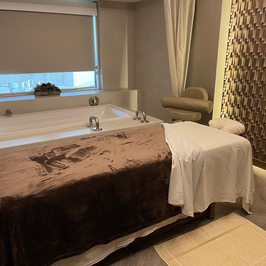 Softly lit treatment suite with a made-up couch beside a deep soaking tub