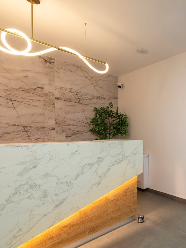 Marble reception desk under a curved pendant light with a potted plant behind