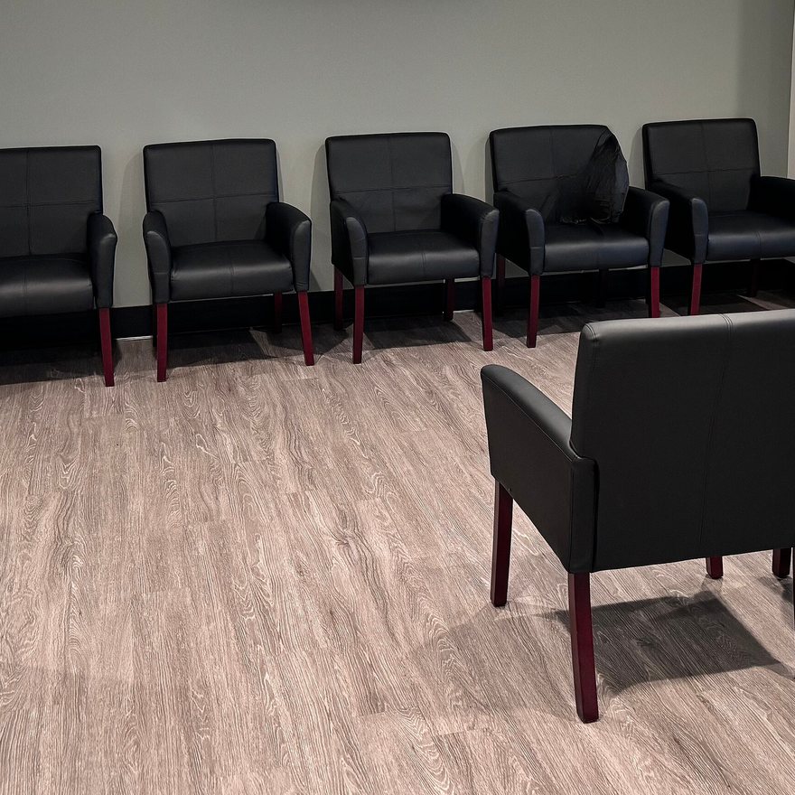 A row of black waiting-room chairs along a pale wall on light wood flooring