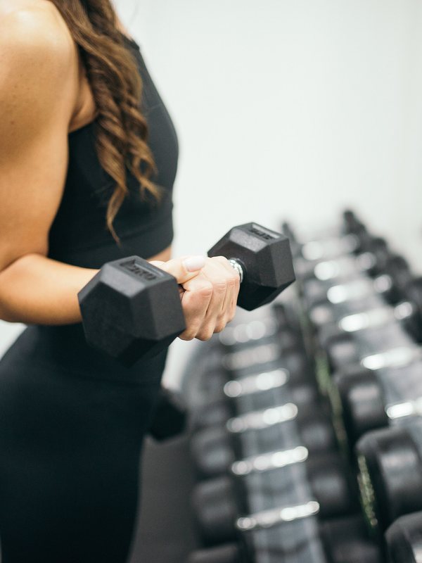 A member curling a hex dumbbell beside the dumbbell rack