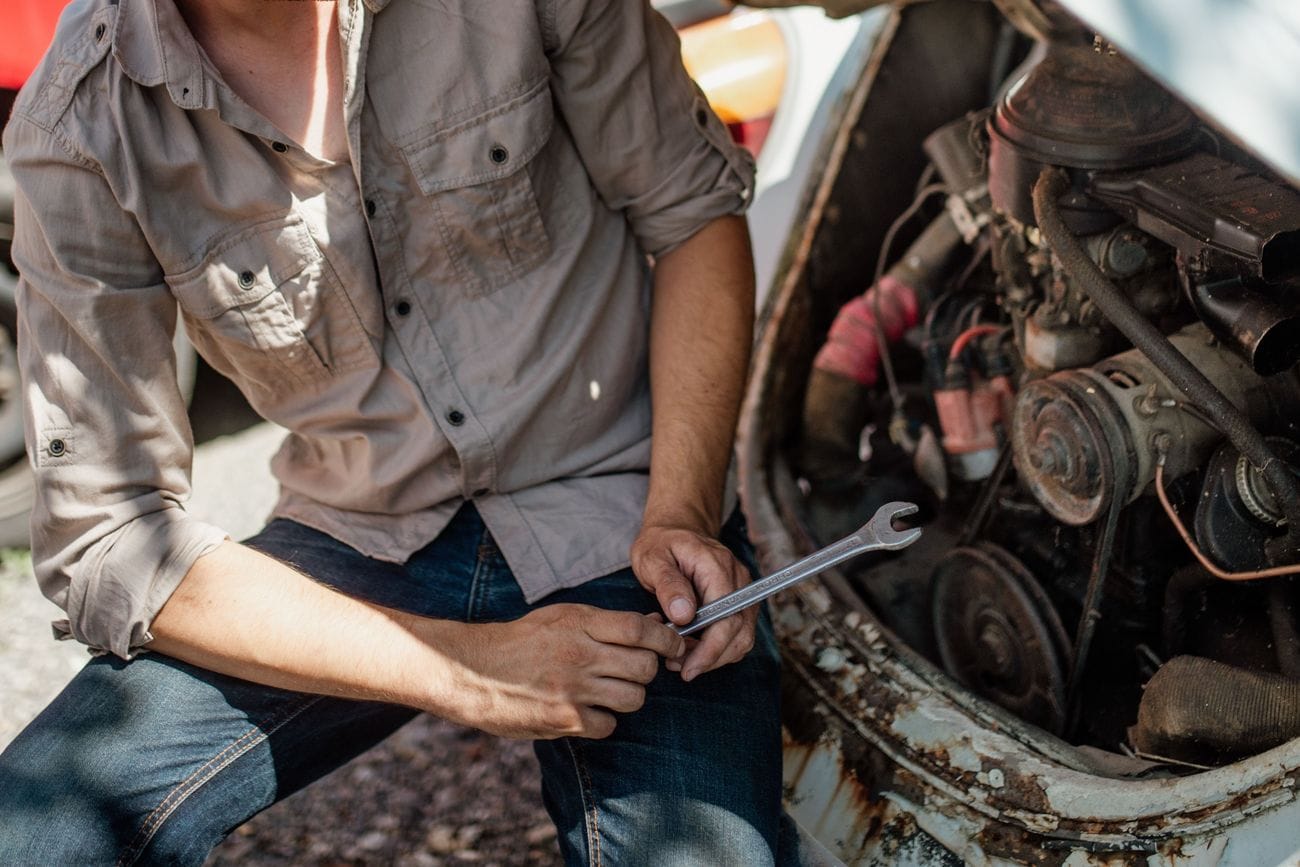 A mechanic's hands turning a wrench on an older engine under an open hood.