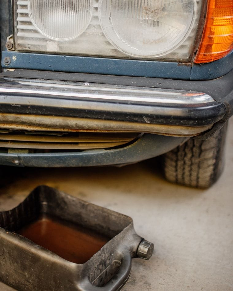 The front of a car in a workshop, with an oil drain pan set on the floor beneath the bumper.