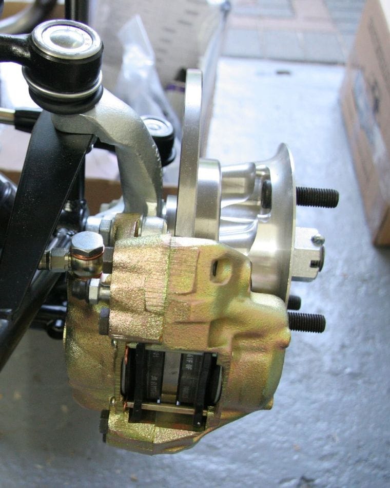 A brake caliper and hub on a car under assembly, with new brake pipes and hoses being fitted and tightened.
