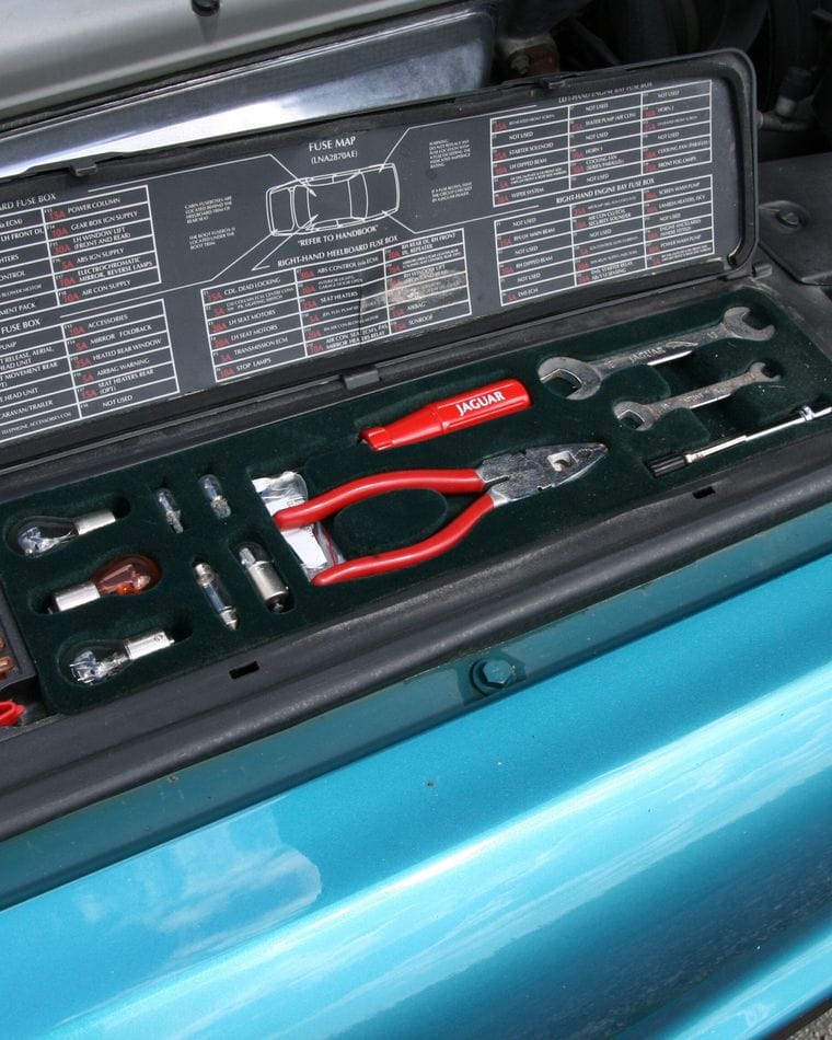A car's original tool kit, with wrenches and a jack handle, stored in its tray inside the engine bay.