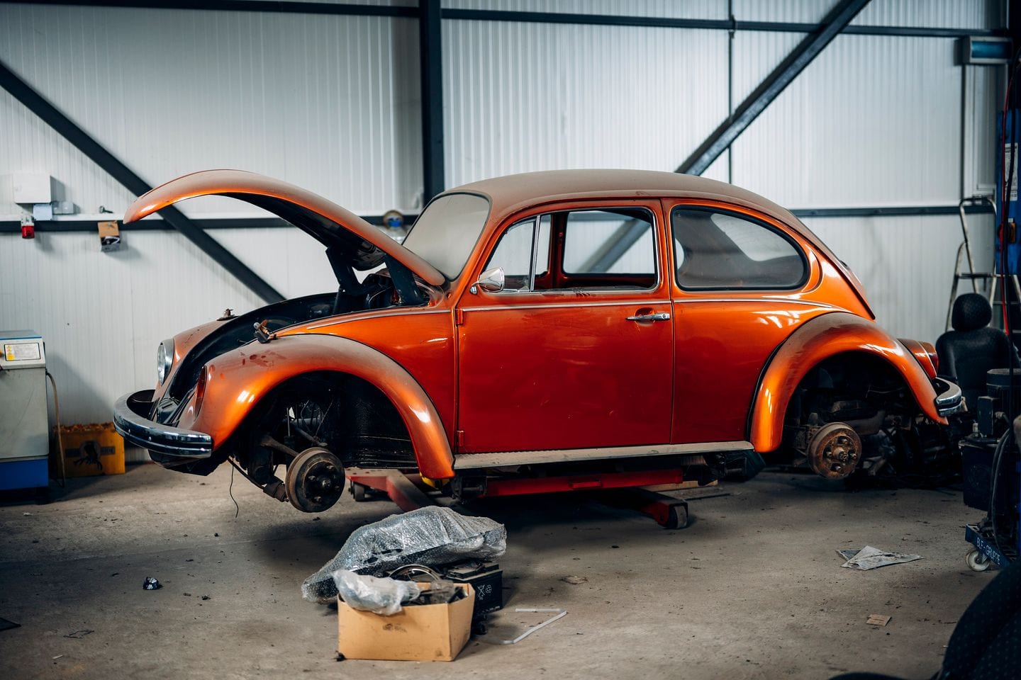 An orange classic car part-way through a restoration in a garage, panels and tools around it