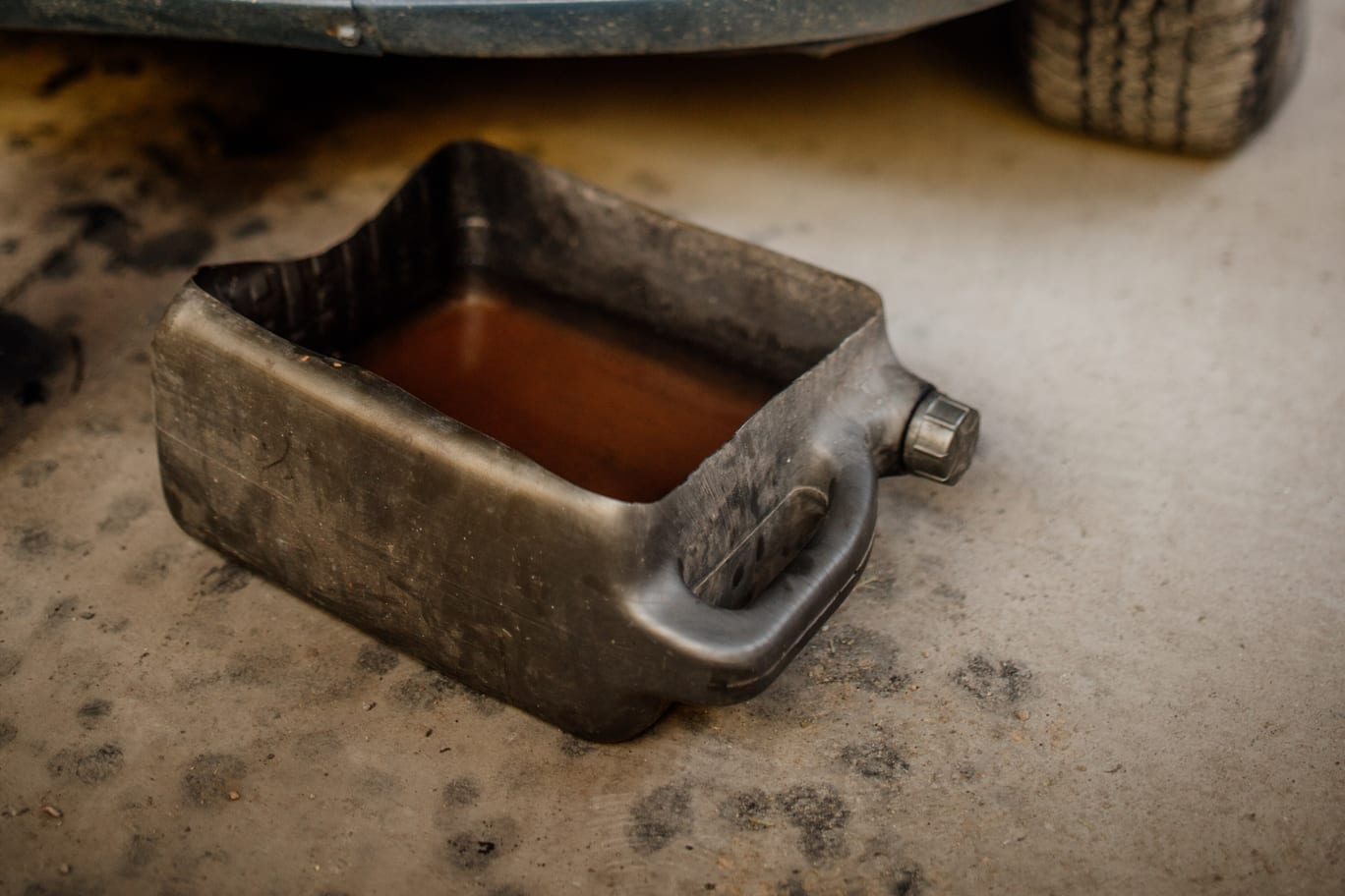A drain pan of used engine oil on the workshop floor beneath the front of a car