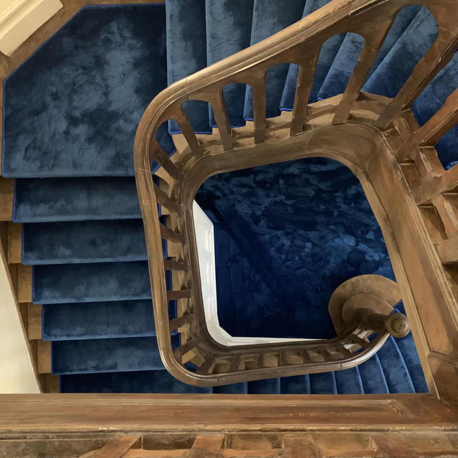 A stair hall with a curving flight, a painted balustrade and daylight falling from above.
