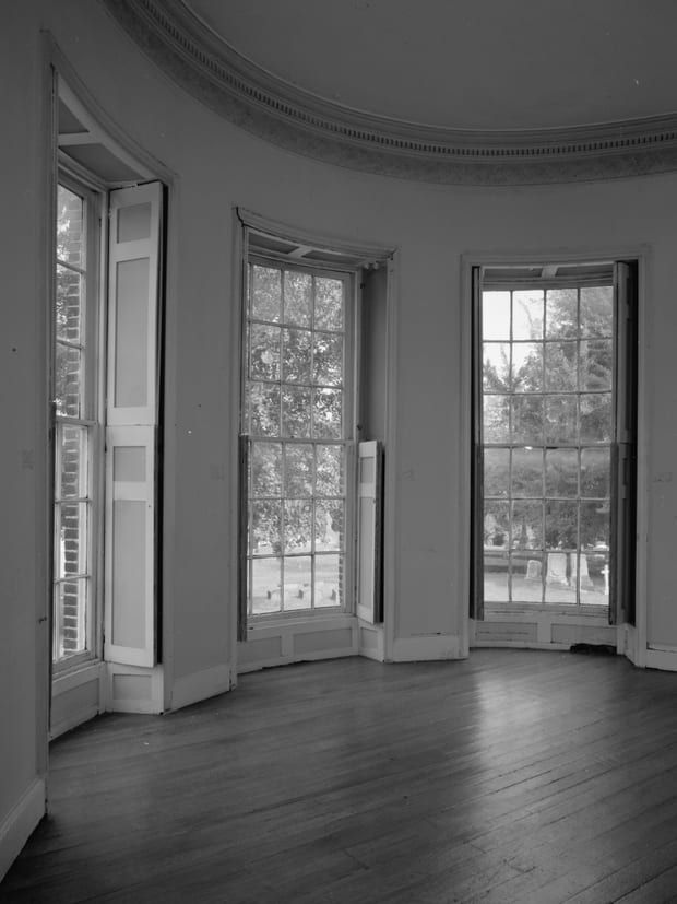A tall window bay with panelled shutters and a bare wooden floor.