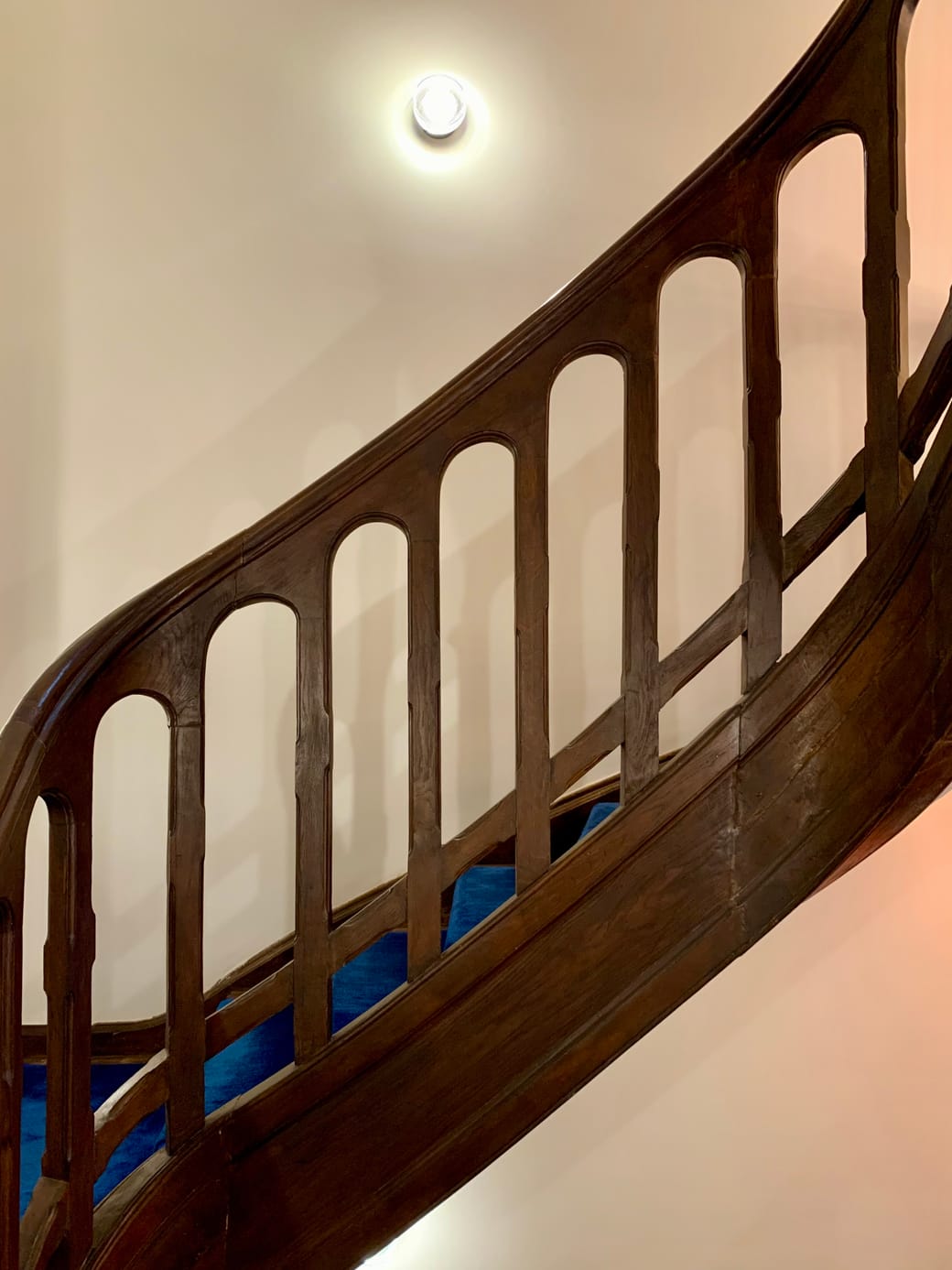 A curving wooden balustrade of arched balusters against a pale plastered stair wall.