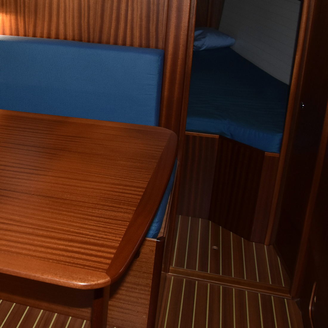 A mahogany table and blue cushions in a yacht saloon, with a berth through the doorway.