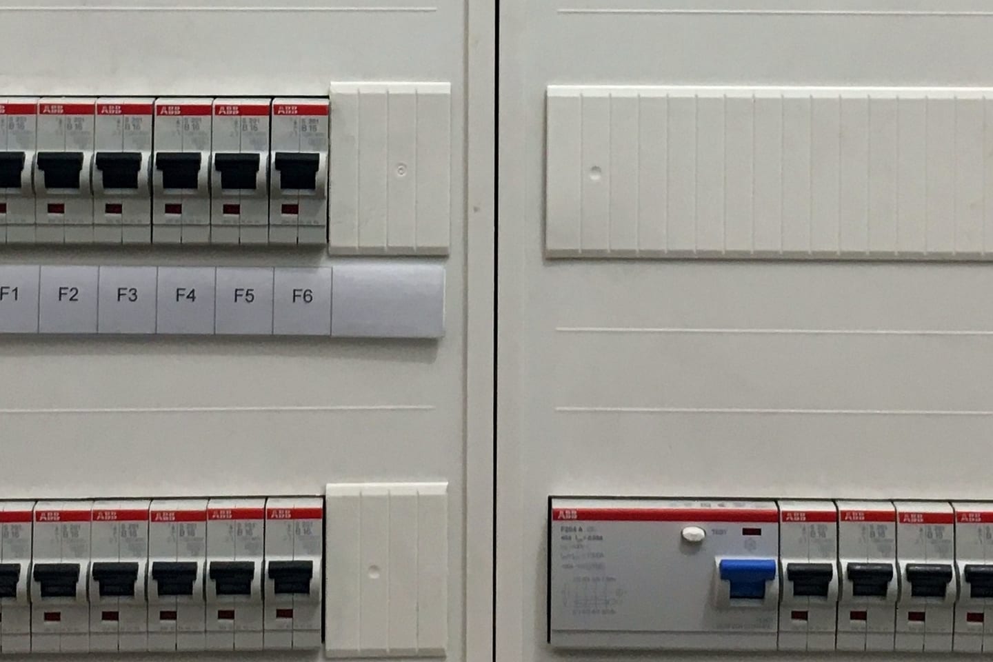 Two consumer units side by side on a wall, one populated with breakers and the other blanked off ready for further circuits.