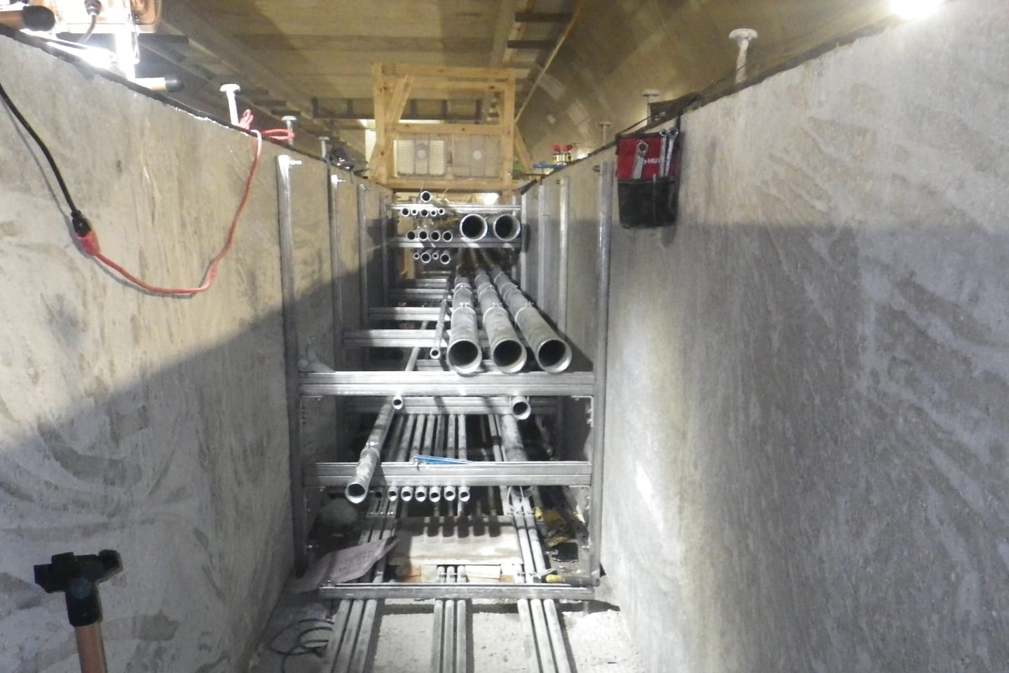 A cable drum and steel support frames set up along a concrete tunnel wall during a conduit installation.