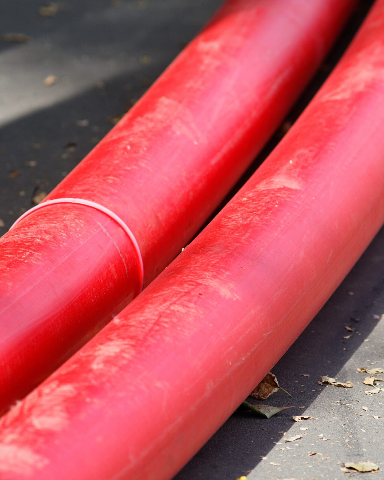 Two lengths of red cable ducting laid side by side across an asphalt surface.