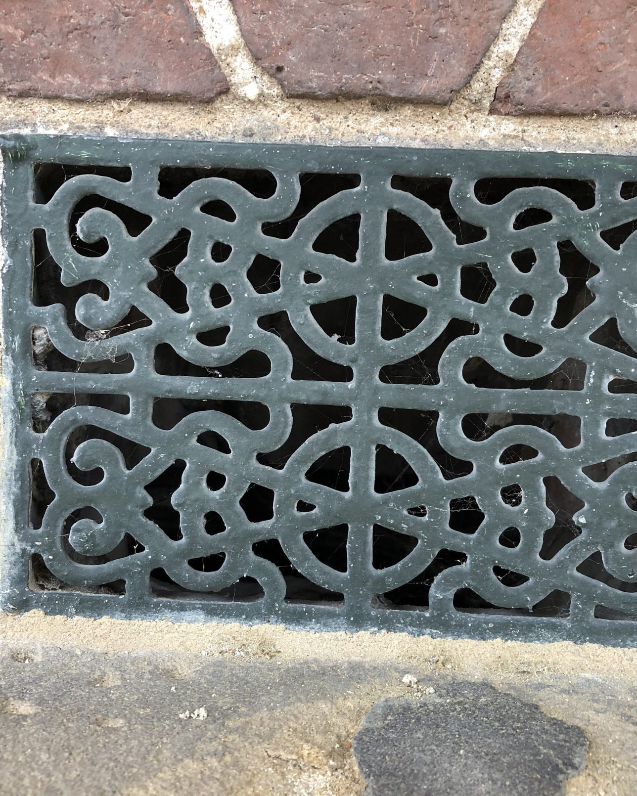 A cast metal air vent set into a stone wall, its louvres worn and open.