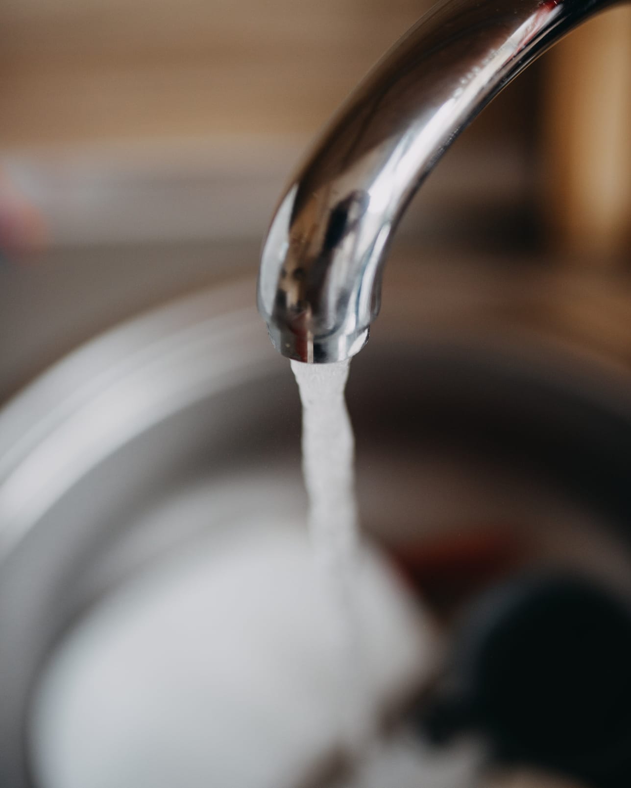 Water running from a modern kitchen mixer tap into a stainless steel basin