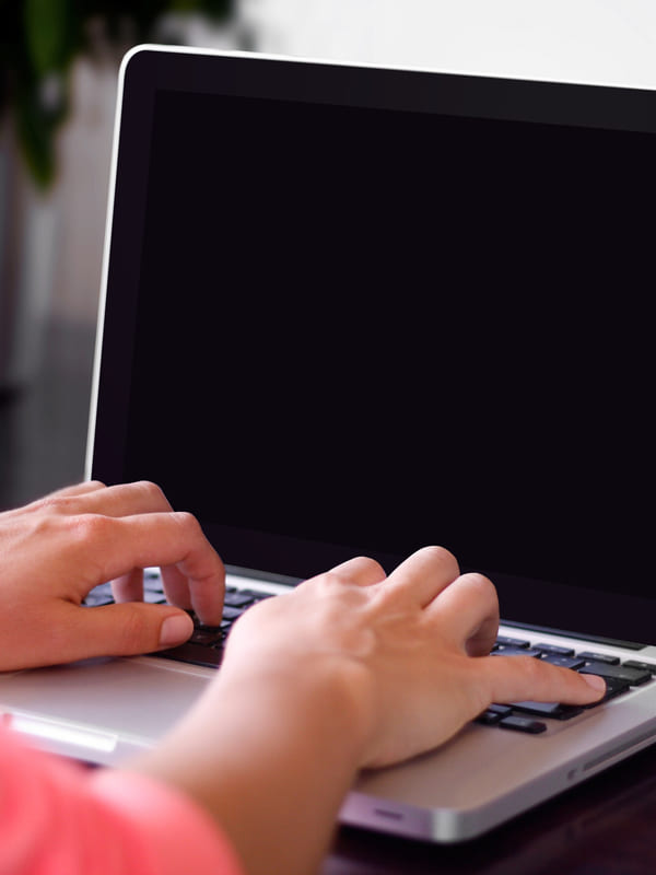 Hands typing on a laptop at a dark desk