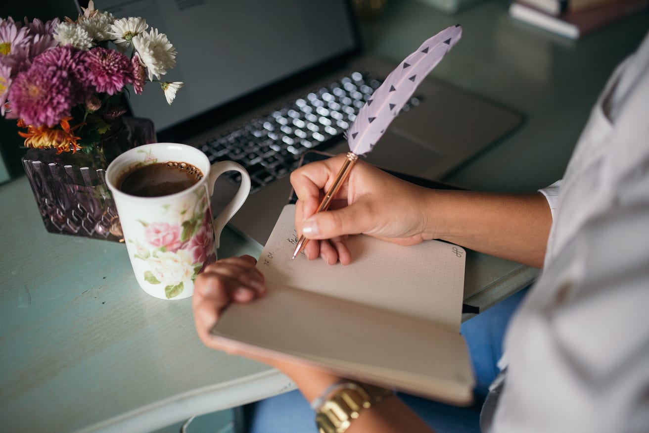 An open notebook and a cup of coffee on a desk, with a pen resting on the page.