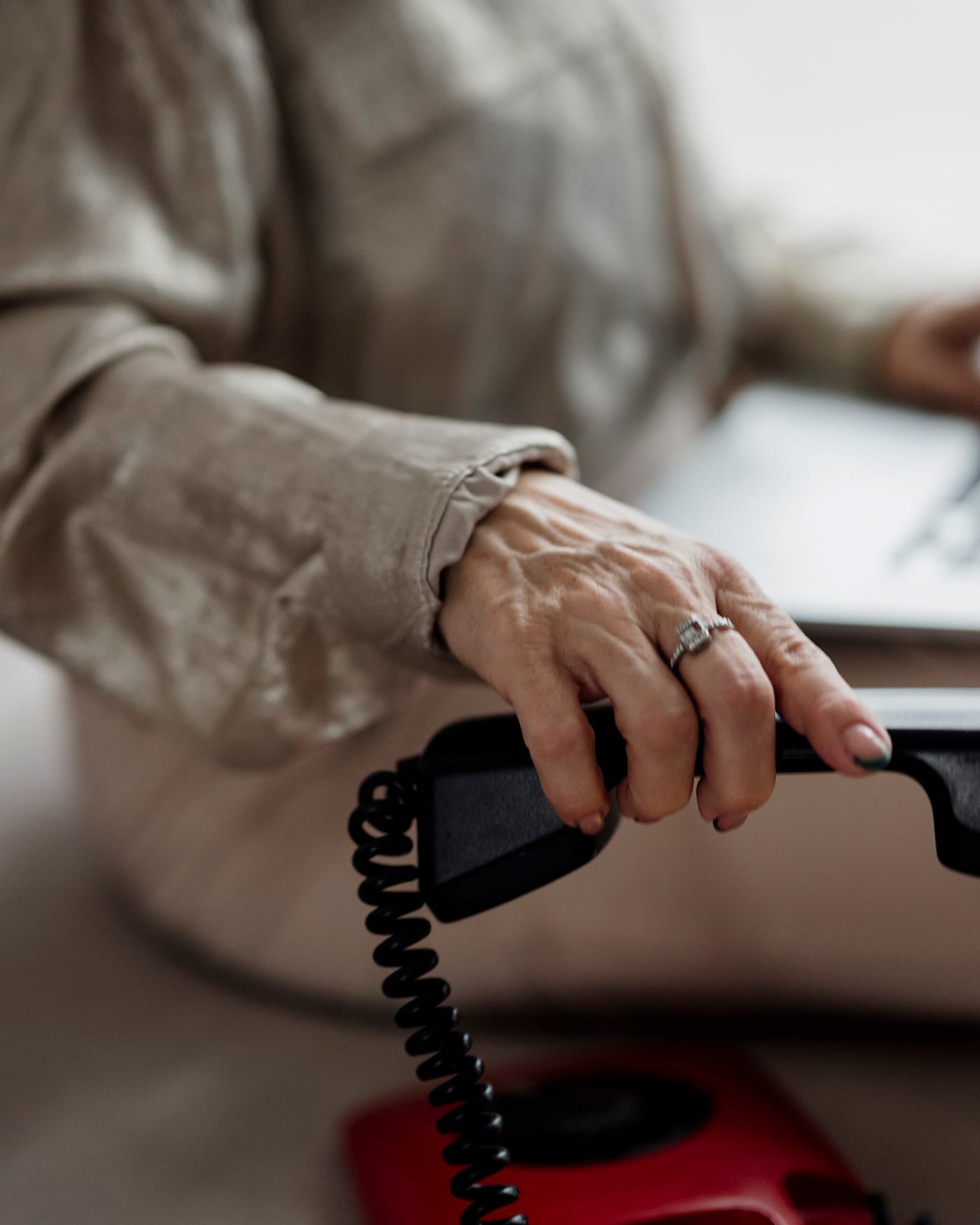 A person using a laptop while holding a telephone receiver, face out of frame.
