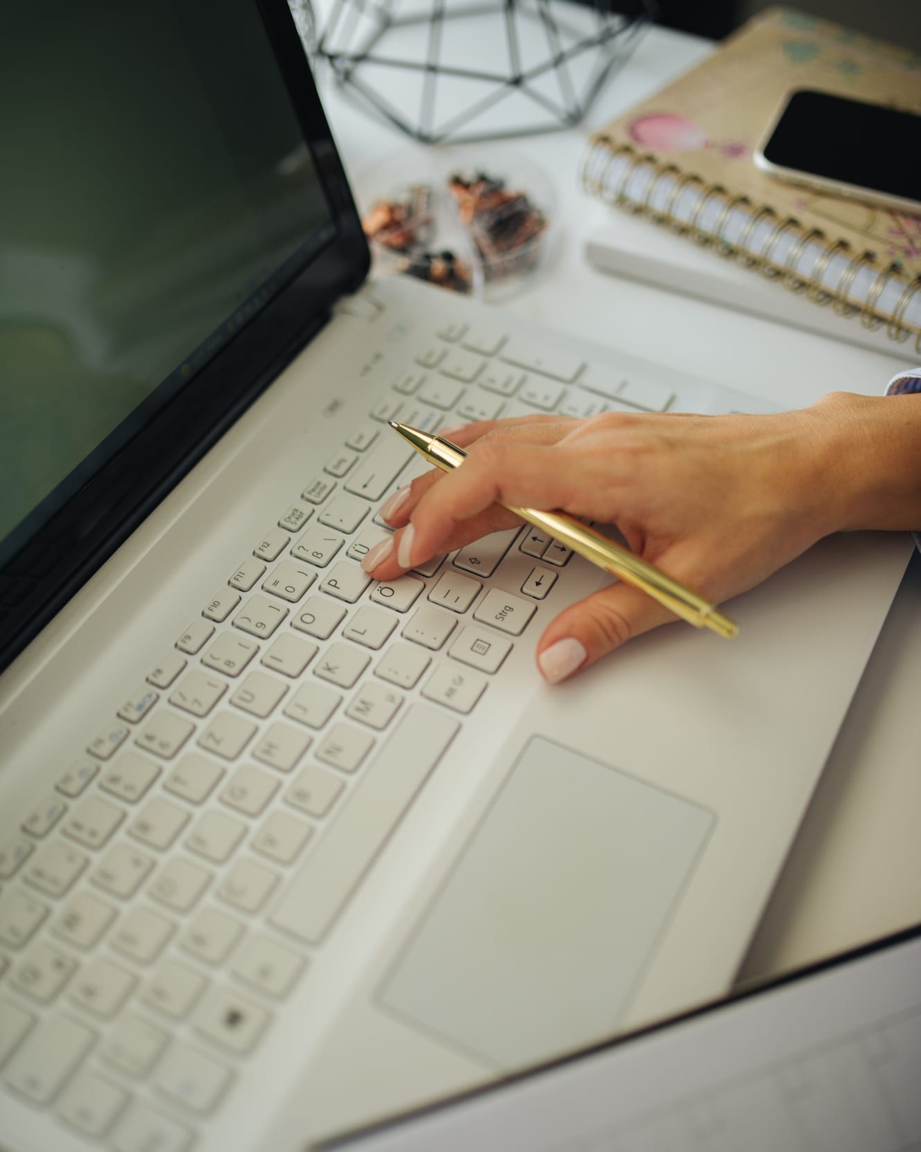 Hands at a laptop beside notebooks, a phone and a gold pen.