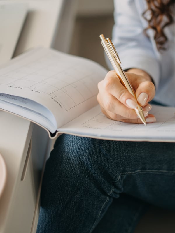 A hand writing into the day columns of a weekly planner with a slim pen