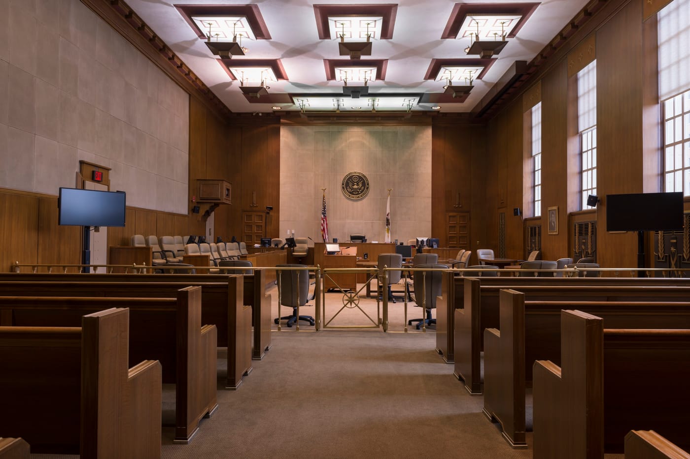 A federal courtroom with wood panelling, a coffered ceiling, the bench and rows of public benches.