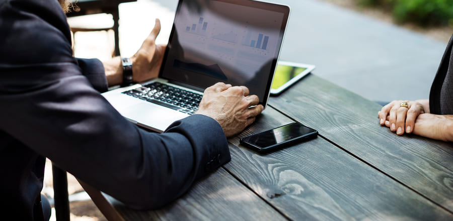 An adviser turning a laptop of charts towards a client across a table, mid-review