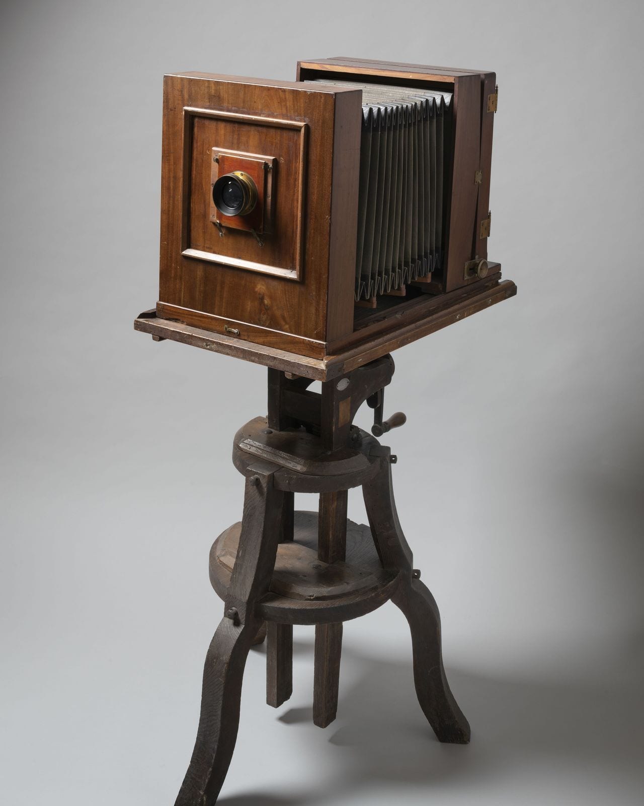 The front standard and lens of a wooden bellows camera on its turned wooden stand.
