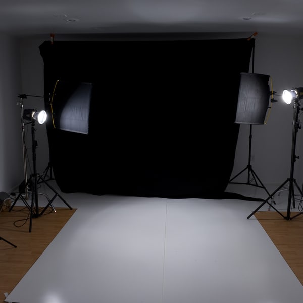 A lit but empty portrait set: black fabric backdrop, two softboxes and white bounce flags