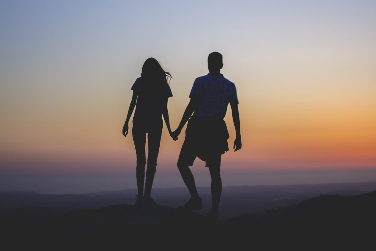 Couple silhouetted hand in hand against a sunset sky