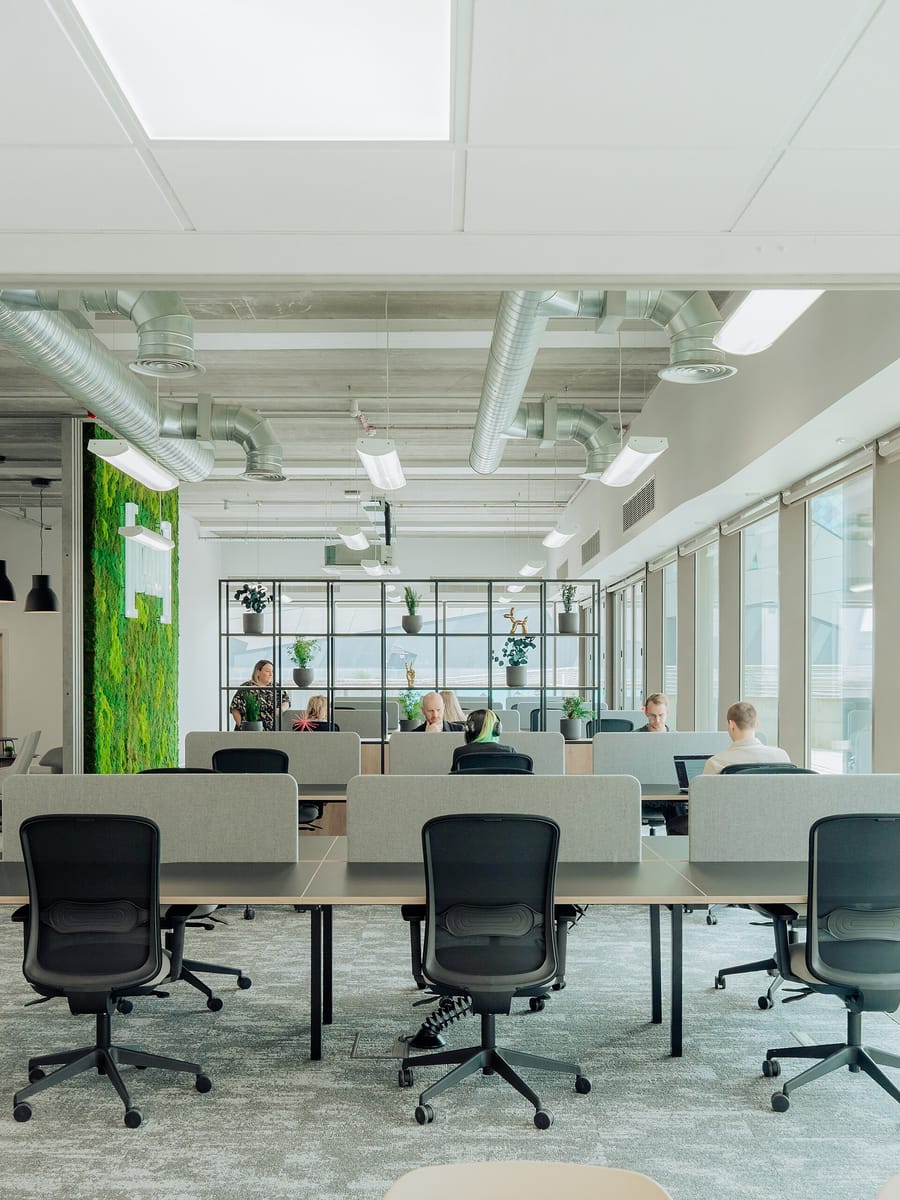 An open coworking floor with rows of desks and task chairs along a wall of full-height windows.