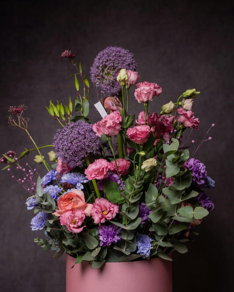 Allium, lisianthus and eucalyptus arranged in a pink ceramic pot against a dark background.