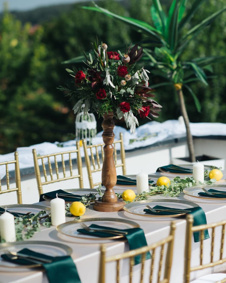 A raised centrepiece of red flowers and green foliage on a dressed event table.